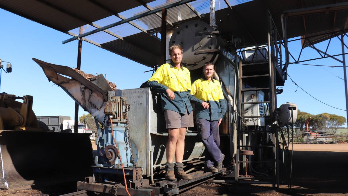 Jason Uyen (left) and Reece Ward at the hopper which feeds some of the spent dried biomass from previous distillations into a furnace that turns water in a tank above it into steam to be pumped through a shipping container packed with green eucalyptus biomass to extract the oil.