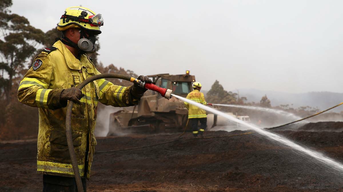 NSW Fire and Rescue officers working to contain the fire at the Eden Chip Mill. Australian Army bulldozers have been used to thin out the smouldering stack. Photo Sgt Max Bree