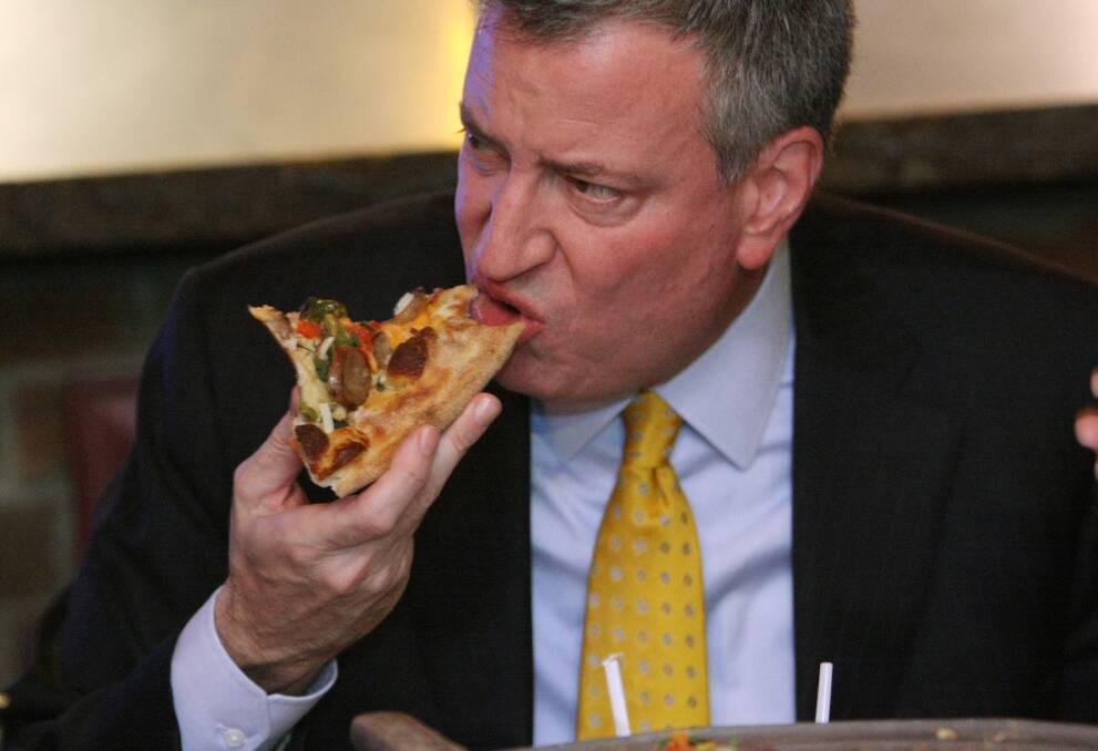 New York Mayor, Bill de Blasio, chomps into a slice of pizza. The pizza contains processed meat which his city council now wants to ban. 