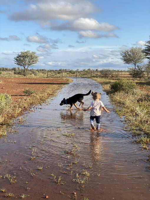 Brydie Hahn and dog Sally play in the puddles after 51mm of rain fell on Friday and Saturday at Burkobulla Station north of Eromanga. Photo: Heather Hahn.